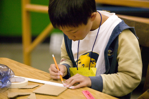 A student is sitting at a desk and drawing with a ruler during a science activity.