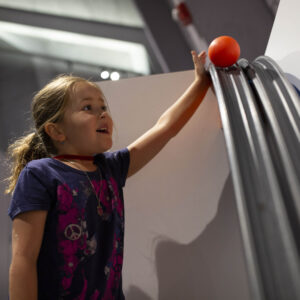 A young child setting a ball at the top of a ramp